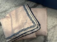 Two soft pink scarves shown together; one smooth with navy floral border and 'Ipekten' embroidered, the other soft knitted pink scarf.