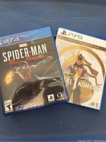 Front cover of Spider-Man Miles Morales for PS4 and Mortal Kombat 1 Premium Edition for PS5 showing case art for both games lying on a blue surface.