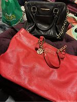 Two purses including a black Steve Madden handbag with gold-tone hardware and a red DKNY handbag with gold-tone chain and charms.