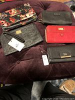 Top view of 5 wallets and clutches on purple surface showing colors, patterns and brand tags