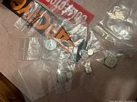 Photo showing assorted vintage watch parts including watch faces, movement mechanics, small gears, and glass face covers in plastic bags on carpet surface.