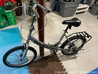 Side view of silver Mongoose folding bike showing frame, handlebars, saddle, pedals, front and rear wheels with rear cargo rack.