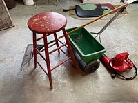All four items in the lot shown together: wooden stool, lawn spreader, leaf blower, and rake on concrete floor