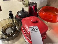 Photo showing red glass pedestal dish, red ceramic covered casserole dish, two amber glass bowls, black and red teapot, salt and pepper shakers.