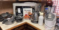 Full kitchen counter view showing microwave, coffee maker, mixer, kettle, cream whipper and ice cream maker with pots and pan in front.
