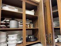 Closed cabinet with shelves showing white ceramic CorningWare dishes, a few pans, and lids.