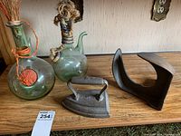 Two green glass decorative bottles and three cast iron items displayed on wooden shelf.