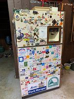 Front view of off-white fridge with built-in ice and water dispenser, covered in many magnets including souvenir magnets and business card magnets.