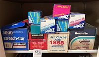 Photo showing multiple boxes including Kirkland stretch-tite plastic wrap, Reynolds foil, Alcan foil, Resinite plastic wrap, and several boxes of Ziploc storage and sandwich bags stacked on shelf.