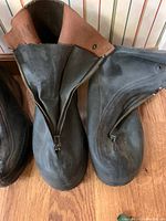 Close-up of two pairs of rubber and leather overshoes with front zippers, showing size and material details.