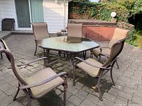 Full view of the hexagonal outdoor dining table with glass top and six metal frame chairs placed on patio.