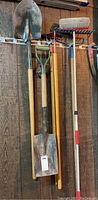 Photo of several garden and snow removal tools hanging on a wooden wall, showing wooden handles and tool heads