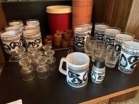Vintage Arctic Canada themed drinking glasses, Canadian Club jug, red and beige ice container, assorted clear glasses, and wooden holders arranged on a shelf.