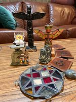 Wide shot of all items on wooden table showing variety of carvings, stained glass piece, plaques, and figurines