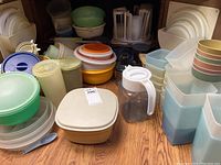 Image showing assorted vintage Tupperware bowls in various sizes and colors with lids, clear pitcher with white lid and handle, and some storage containers assembled on the floor.