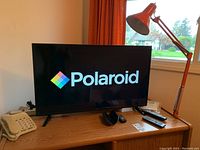 36-inch Polaroid TV on wooden desk accompanied by vintage orange desk lamp and beige telephone.