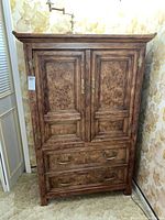 Front view of wooden vertical storage cabinet showing two paneled doors and two drawers with brass handles.