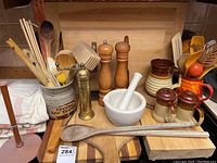 Overview of wooden and ceramic kitchen utensils including spoons, cutting boards, grinders, mortar and pestle, and ceramic containers.