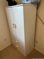 Front and side view of the white laminate cabinet showing double doors and two drawers with gold handles.