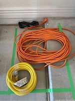 Four electrical extension cords coiled on the floor. Orange cord, yellow cord, black cord, and short orange cord visible.
