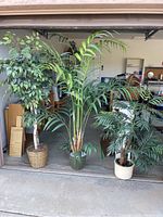 Three faux plants: one ficus tree in wicker pot, two tall faux palms in ceramic pots.
