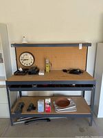 Full view of the metal and wood workbench with pegboard, drawer and various items placed on shelves and pegboard.