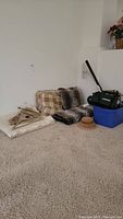 Wide view showing grouped items on carpet including vacuum, hangers, blankets, pillows, and coasters.