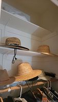 Shelf with multiple straw hats in natural shades, one with chin strap, also some fabric hats visible below.