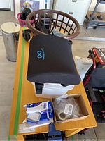 Full overview of medical supplies including black mesh cushion pillow, brown plastic laundry basket, Sony headphones, box of adhesive tape, and various medical items.