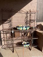 Full view of large metal porch stand with shelves, decorative scrollwork, and some objects placed on it for scale.