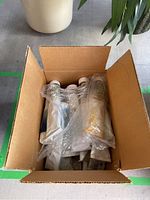 Open cardboard box with multiple tubes of oil paint wrapped in plastic inside, visible tube colors and labels.