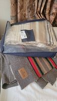 Two Pendleton blankets shown folded and stacked, one in a clear zippered bag with stripes in beige and brown shades, the other gray with colorful stripe accents and a leather label.