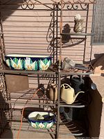 Metal shelf display of two colorful ceramic plant troughs with floral patterns, several watering cans, and solar garden lights.