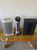 Three space heaters displayed on a wooden table against a blank wall: Patton, Pelonis, and Winix Plasmawave models.