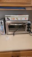 Toaster oven, mandoline box, and Aroma hot plate displayed on countertop.