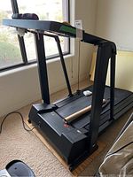 Photo of black Weslo treadmill folded up near a window showing handrails, display console with control buttons, attached power cord, and pink hand weights on console.