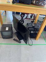 Two televisions and one printer under a table, including a small portable TV, a flat-screen HDTV, and an HP Photosmart printer with remote control on top.