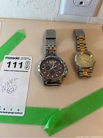 Two men's watches side by side on a countertop, one Stuhrling chronograph with broken band, one gold and silver toned half dollar watch.