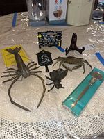 Set of four items displayed on lace tablecloth. Includes brass crab, brass lobster, metal fly napkin holder, and boxed letter opener.