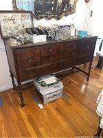 Front view of vintage wooden buffet sideboard showing drawers, metal circular pulls, and turned legs with stretcher base. Items on top not included.