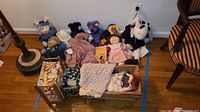 Wide photo showing the entire lot laid out on the floor including dolls, plush toys, wooden doll crib and bunk beds, and blankets