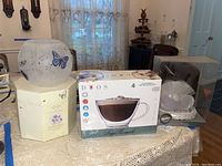Full shot of Lenox Butterfly Meadow rose bowl, Duos latte and cappuccino cup set box, and anniversary cake topper in clear box on table with lace cloth.