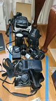 Full lot arranged on floor showing multiple cameras, camera cases, lenses, and a cylindrical container possibly for film or lens storage