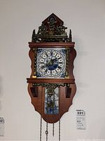 Front view of Dutch-themed wall clock showing blue and white dial with windmill and boat scene, wooden frame, brass-tone filigree.