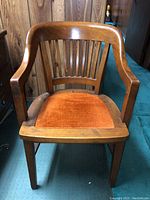 Front view of wooden desk chair showing orange fabric seat and spindled backrest.