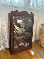 Full view of a wooden display cabinet with glass door, containing various salt and pepper shakers inside on multiple shelves.
