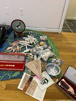 Overview of lot showing seashells, coral, folding fans, decorative cat plate, combs, and blade in boxes spread on a patterned cloth on floor