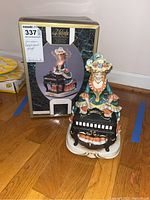 Photo showing the figurine with its original box, labeled Melody in Motion Madame Harpsichord Player, hand-painted porcelain bisque finish musical figurine.