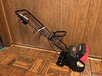 Side view of black and red Yard Machines SnowFox snow thrower showing handle and wheels.