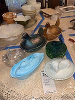 Photo of six vintage covered dishes including carnival glass chickens, lamb, dolphin gravy boat, and Lenox bunny dish